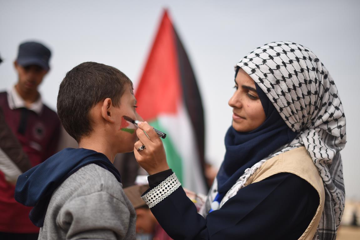 A woman paints a Palestinian flag on a boy's face
