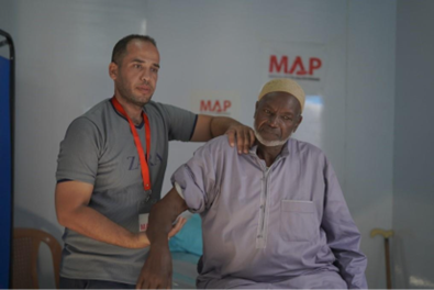 An older Palestinian man receives physio on his shoulder from a medical professional.