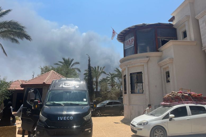 People load cars as they prepare to evacuate the polyclinic. In the near distance smoke is rising from a recent strike.